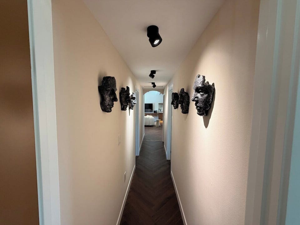 Step into sophistication in this elegant hallway, featuring striking wall-mounted face sculptures and rich, dark herringbone flooring that leads the way through your home.