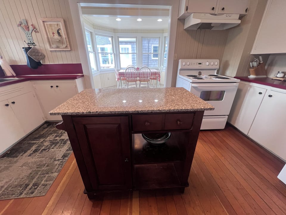 Step into your cozy kitchen with warm wooden accents and modern appliances. The space invites you to prepare meals while natural light streams through charming windows overlooking neighboring buildings.