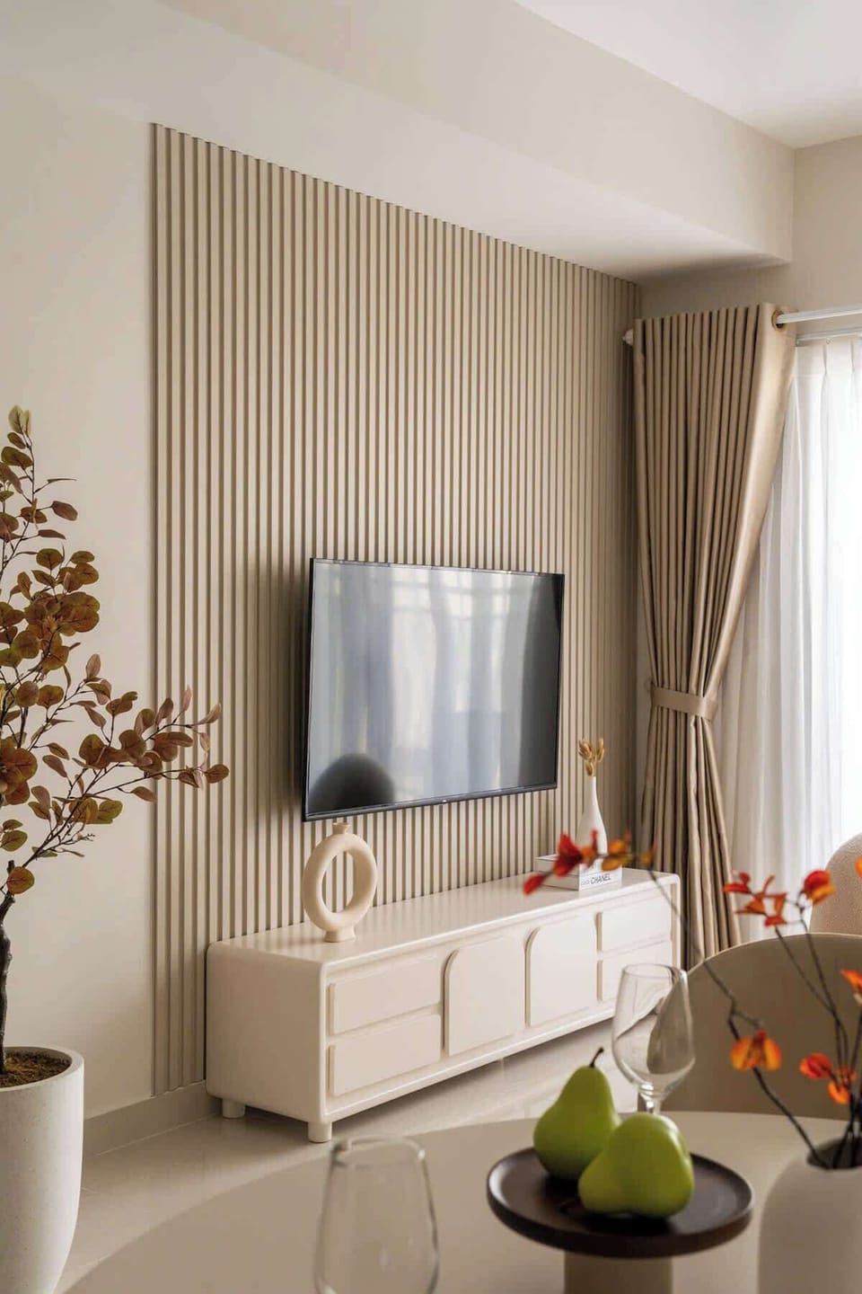 Entertainment area with mounted smart TV, high-speed Wi-Fi, and modern media console. Neutral tones, vertical wood paneling, and full-length blackout curtains create a cozy space to relax or stream your favorite shows.