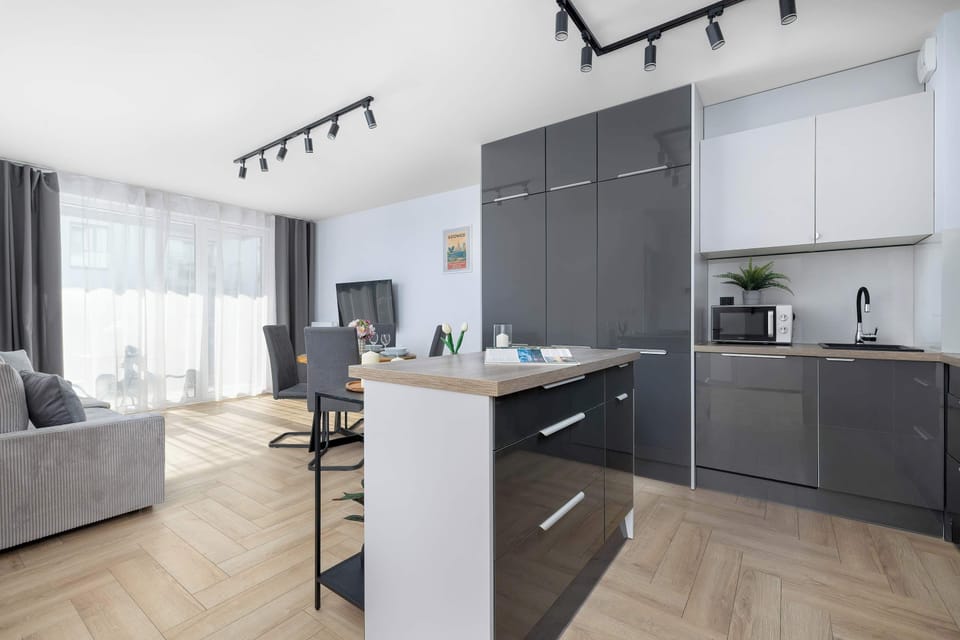 Dark grey kitchen cabinets stand out beautifully against the lighter wooden flooring in this open-plan design. A functional island separates the cooking area from the bright living room.