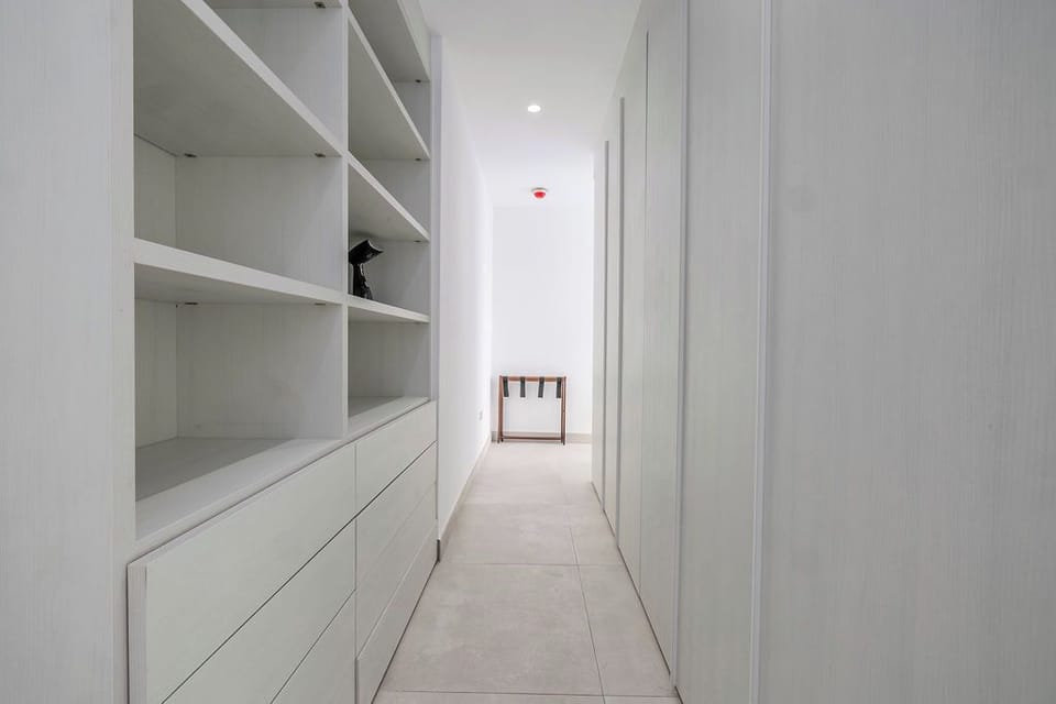 Walk through a bright hallway featuring custom built-in storage and open shelving, perfect for organizing your belongings during your stay in this minimalist, thoughtfully designed space.