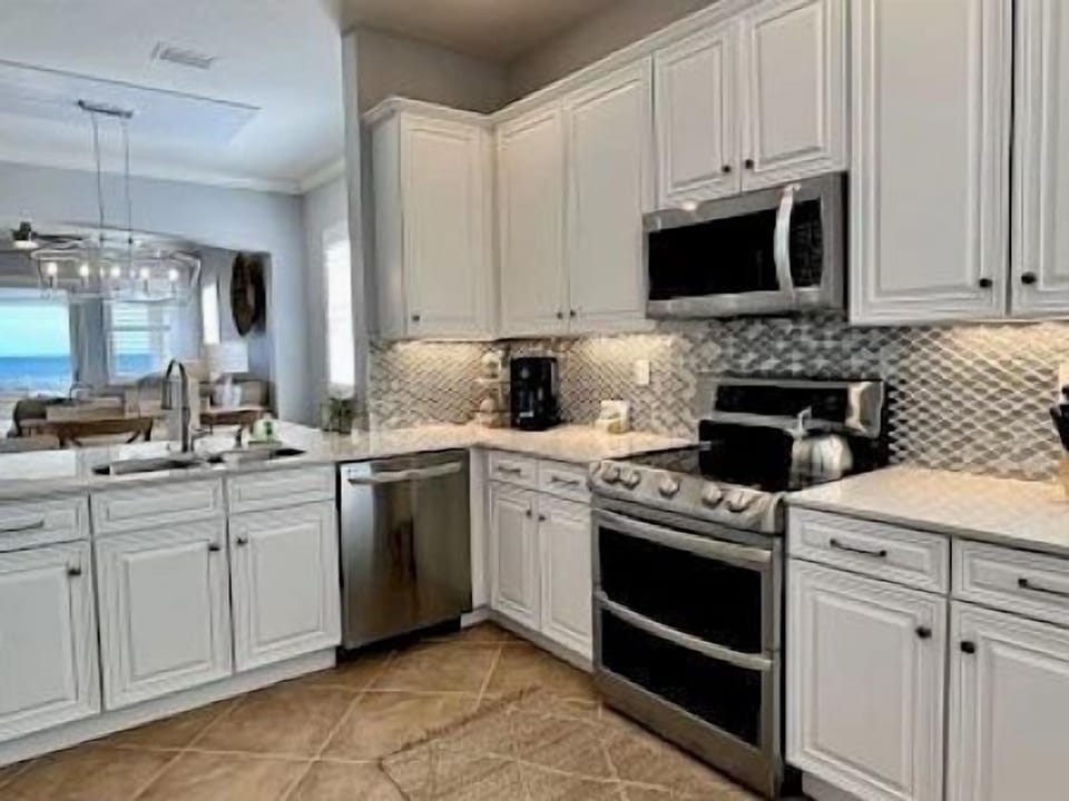 Kitchen with white cabinets, marble countertops, silver appliances, and a tile backsplash