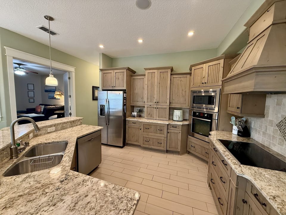Kitchen with light green walls, warm wood cabinetry, granite counters, and an open connection to the living area