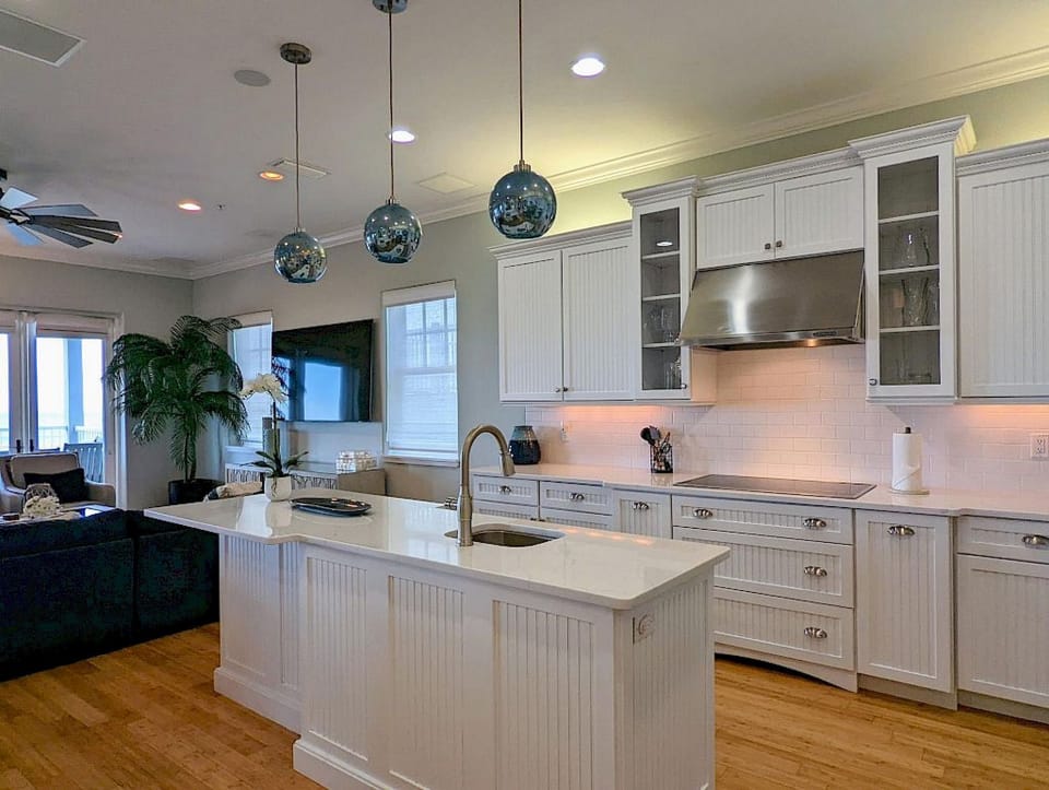 Kitchen with white beadboard cabinetry, island with sink, blue pendant lights, and bamboo flooring