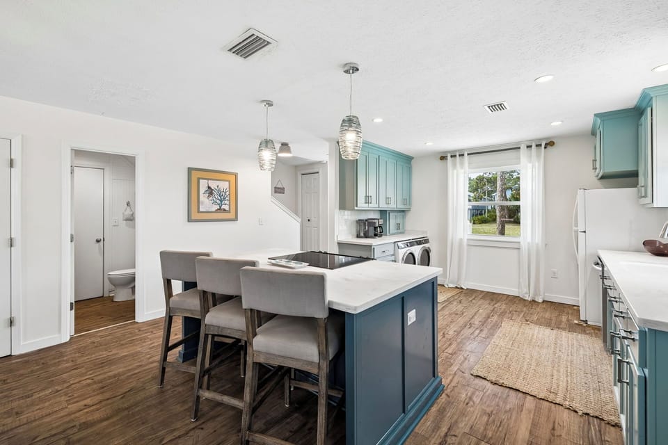 Step into a bright, inviting kitchen where coastal charm meets modern convenience. Gather around the spacious island for morning coffee or casual meals, with natural light streaming through the window and everything you need within reach.