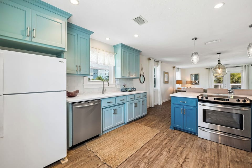 Your fully equipped kitchen blends coastal charm with modern convenience, featuring bright blue cabinetry, stainless steel appliances, and an open flow into the living space where you'll love cooking and gathering.