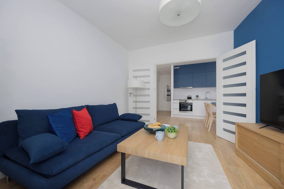 A stylish bedroom with a blue sofa, wooden coffee table, and a TV mounted opposite the seating area. The open layout creates a spacious and comfortable environment.