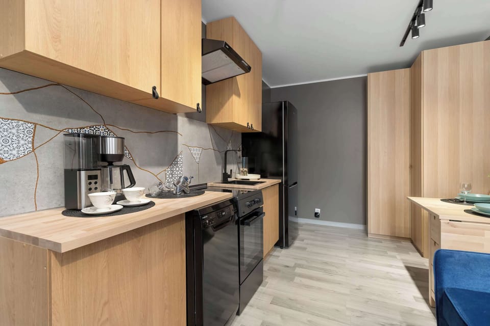 An angled perspective of the kitchenette showcases modern wooden cabinetry and dark countertops. A black oven and coffee machine add functionality to the sleek culinary design.