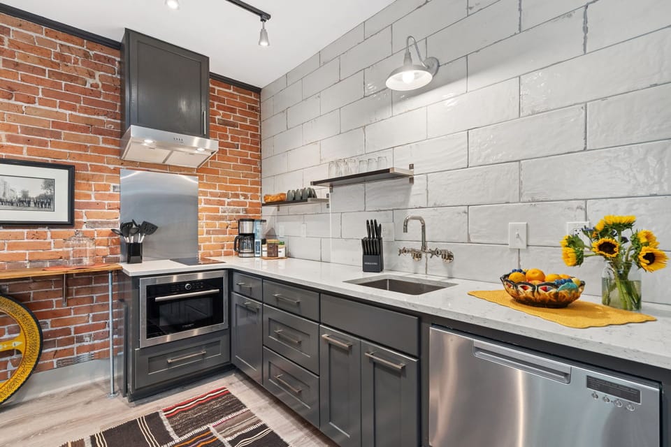 Step into this stylish kitchen where exposed brick meets sleek modern design. Prepare your favorite meals surrounded by bright white subway tile, gleaming countertops, and cheerful sunflowers.