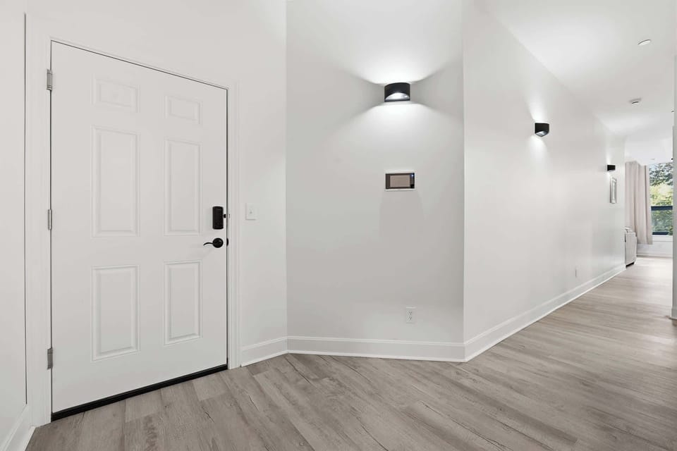 Grand Foyer Entrance | Welcoming entryway with sleek finishes and sconce lighting, opening into the hallway toward the living space.