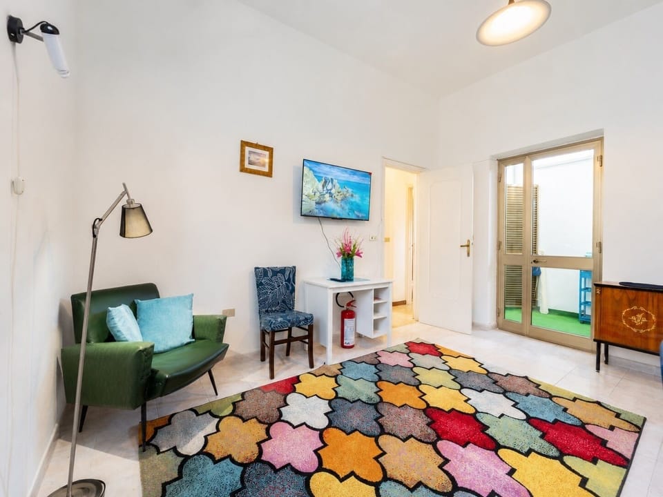 Bright lounge with colorful rug, TV, and balcony access