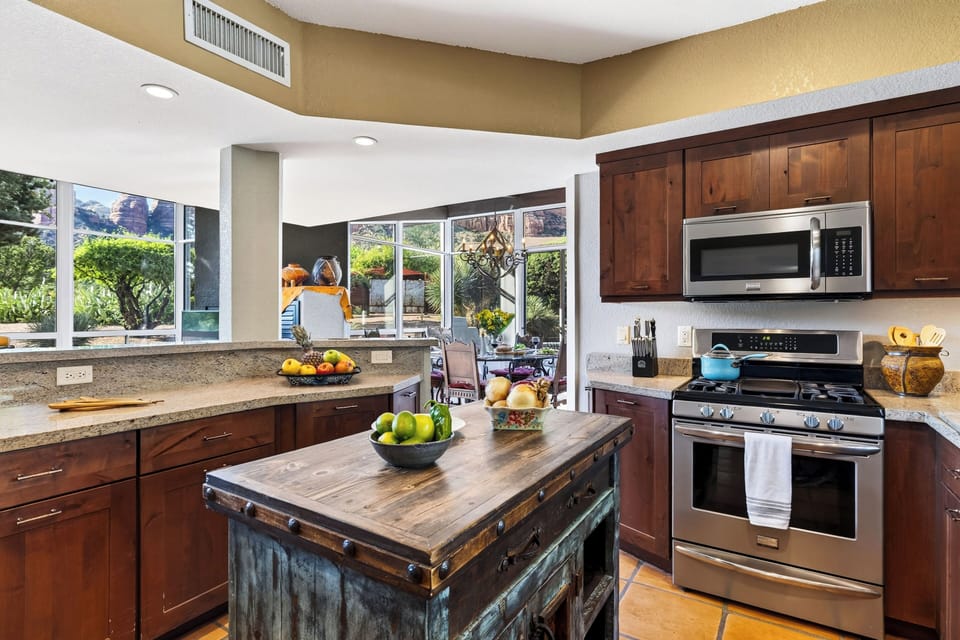 A rustic prep island anchors the kitchen, with stainless steel appliances and red-rock glimpses beyond the adjoining dining area.