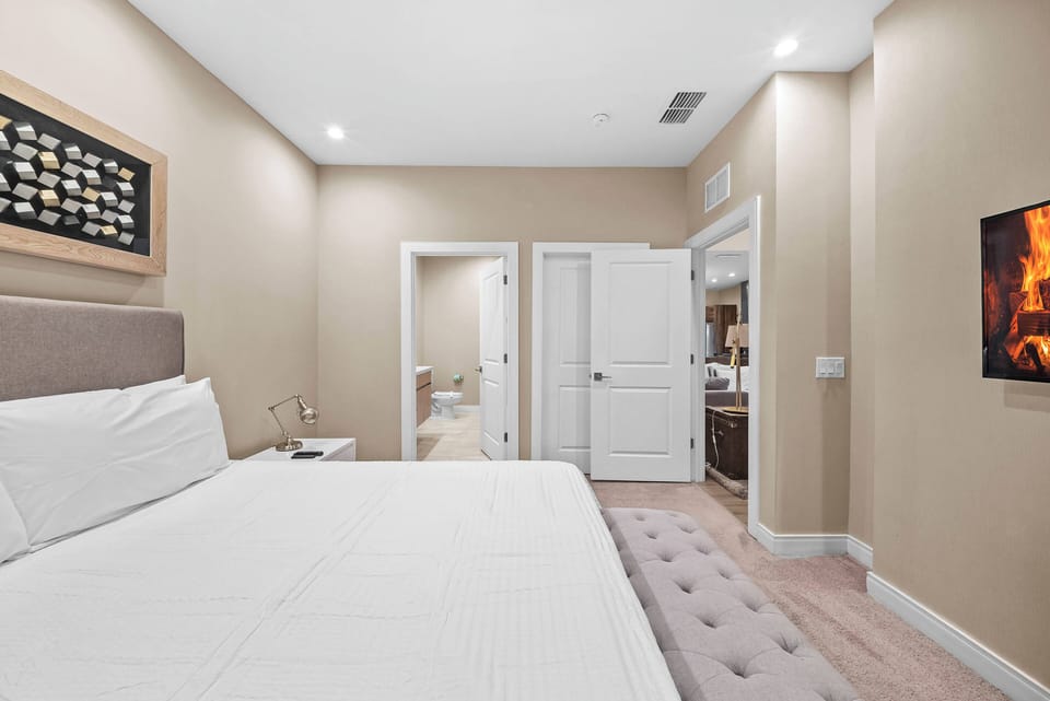 This cozy bedroom features a plush, upholstered headboard and soft, neutral tones that create a relaxing ambiance. Enjoy the convenience of a mounted flat-screen TV for entertainment and easy access to the adjoining bathroom.
