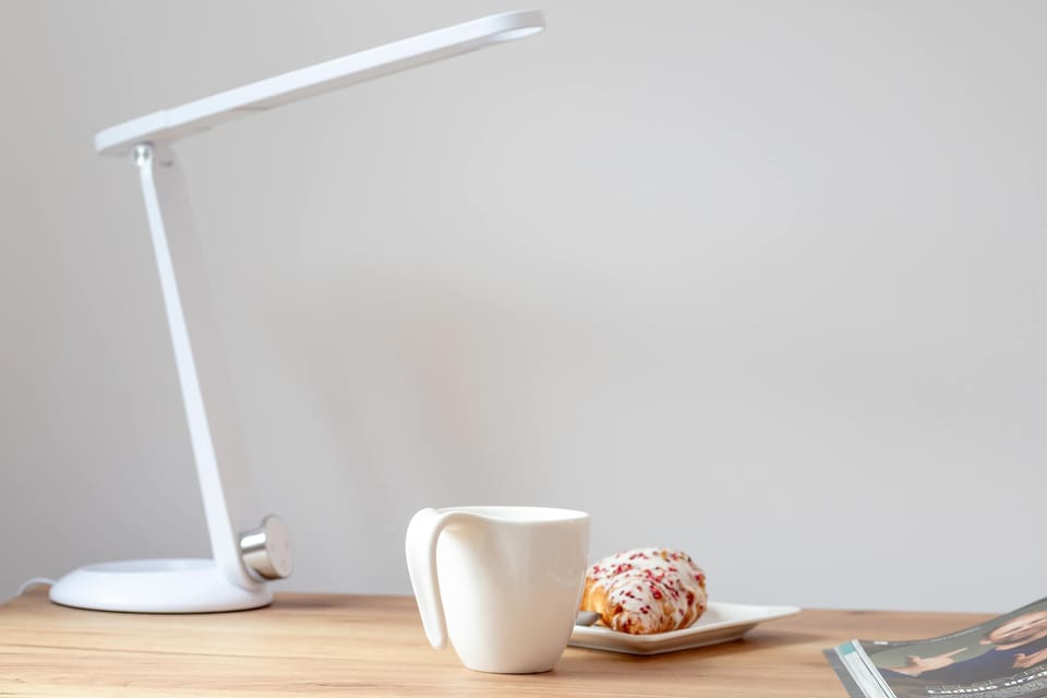 A close-up of a modern desk lamp and coffee cup creates a cozy workspace scene. Simple decorative details add warmth to the interior.