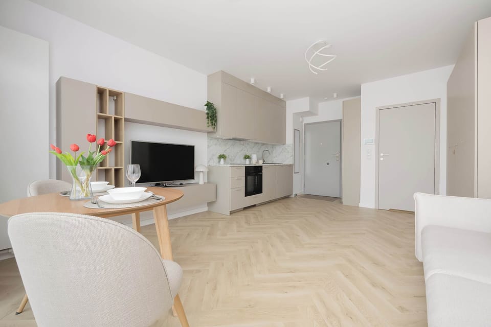 A bright open-plan room with a sofa, dining table, and fully equipped kitchenette.
