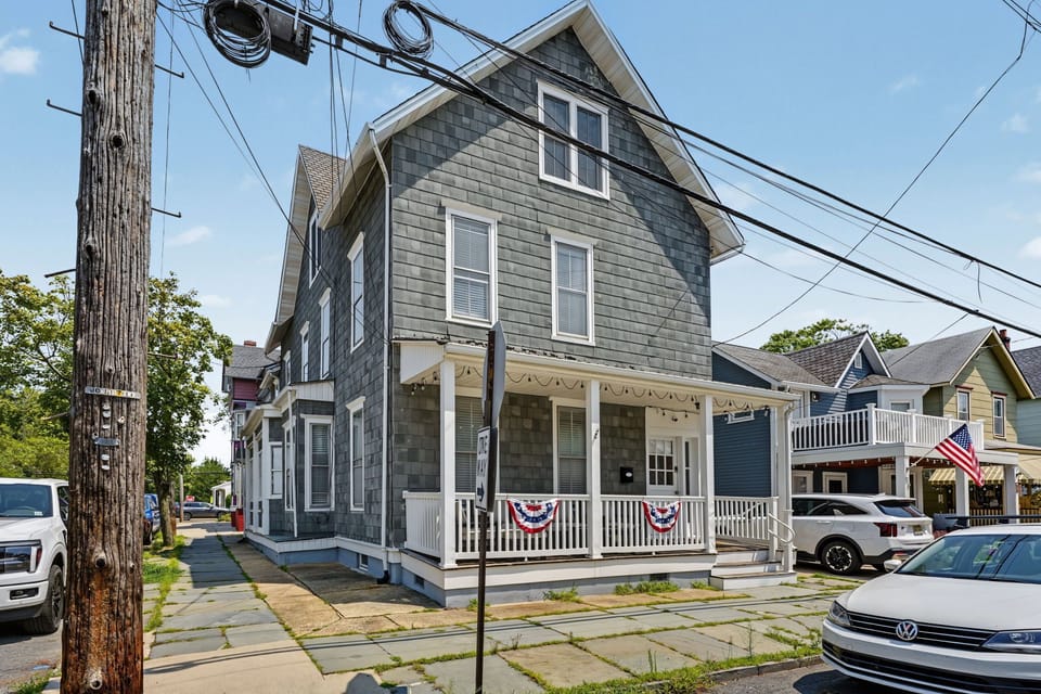 This massive 3-level, 6-bedroom, 3-bathroom coastal estate offers the perfect high-capacity group getaway, featuring a charming covered front porch, timeless cedar shake siding, and unmatched neighborhood walkability just steps from local attractions