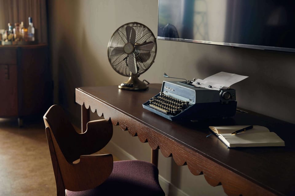 Mahogany desk with a vintage typewriter and decorative fan, set beside large windows framing city views