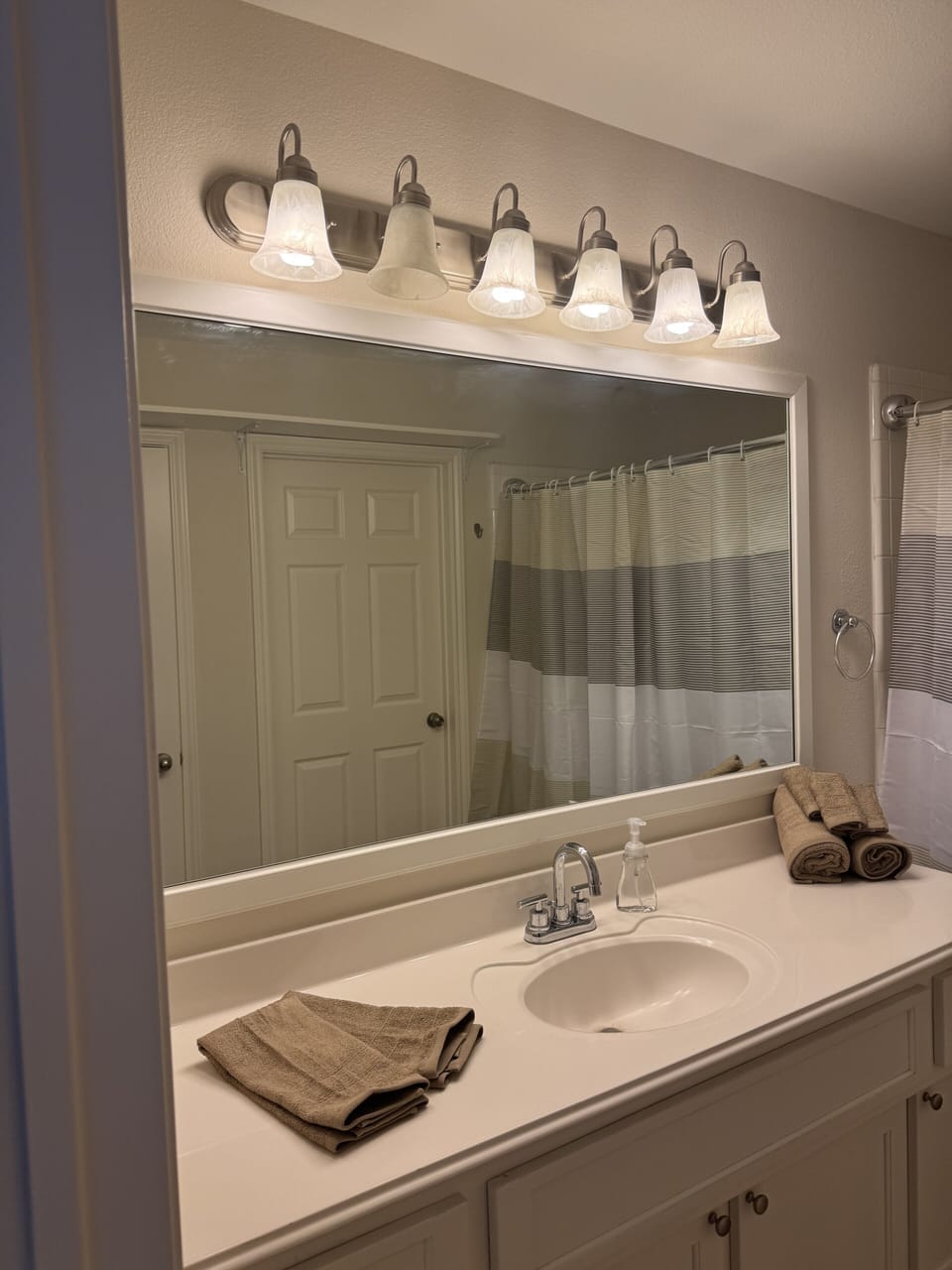 Bright bathroom vanity with large mirror, warm lighting, and ample counter space
