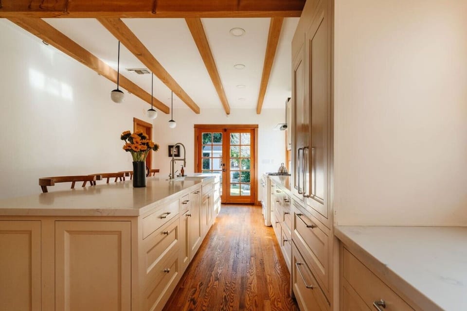 Stunning chef`s kitchen featuring soaring beamed ceilings, a generous center island, pendant lighting, and French doors opening to the outdoors.