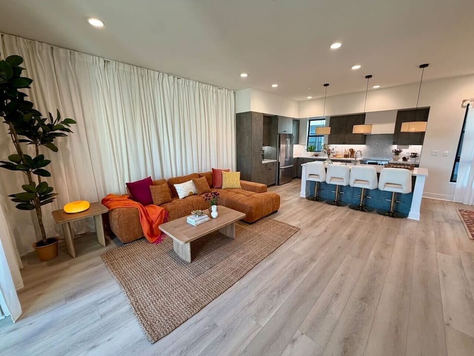 The rust-toned sectional and jute rug anchor a living space that flows seamlessly into the kitchen.