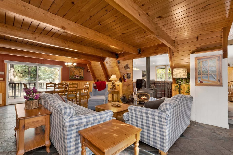 Spacious open concept living room/dining area with tongue in groove ceilings, exposed beams, a cozy wood stove and plenty seating