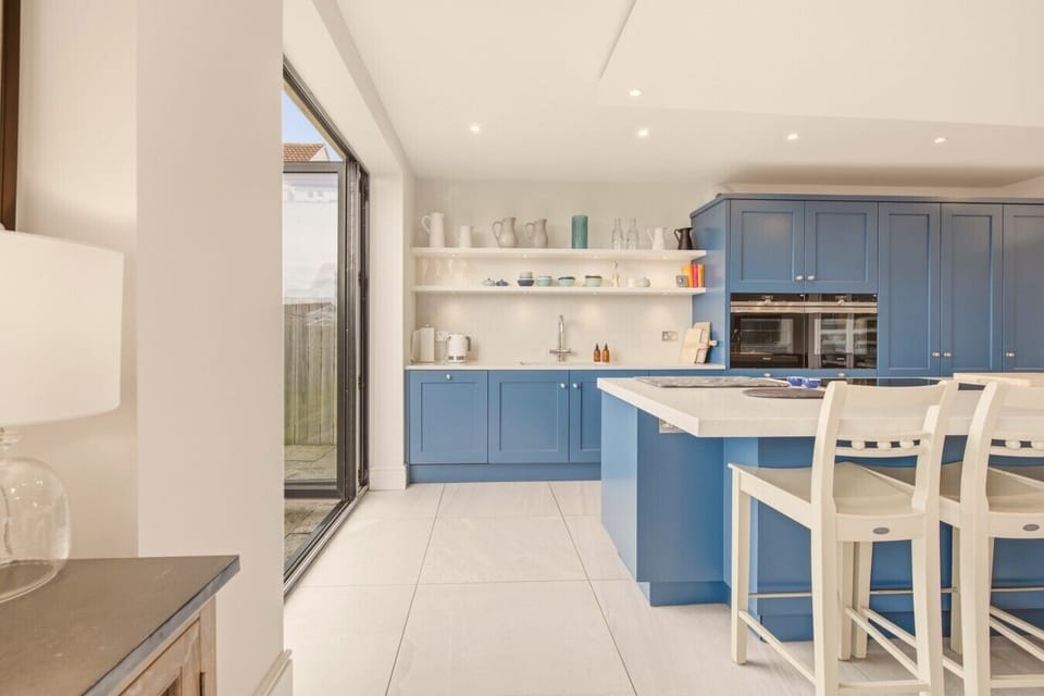 Breakfast bar with white stools, blue kitchen units and open display shelving