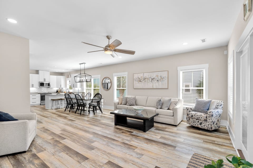 Step into your spacious open-concept haven where natural light pours through tall windows, warming the rustic wood floors beneath your feet. Gather around the inviting dining table or sink into plush seating—your perfect retreat awaits.