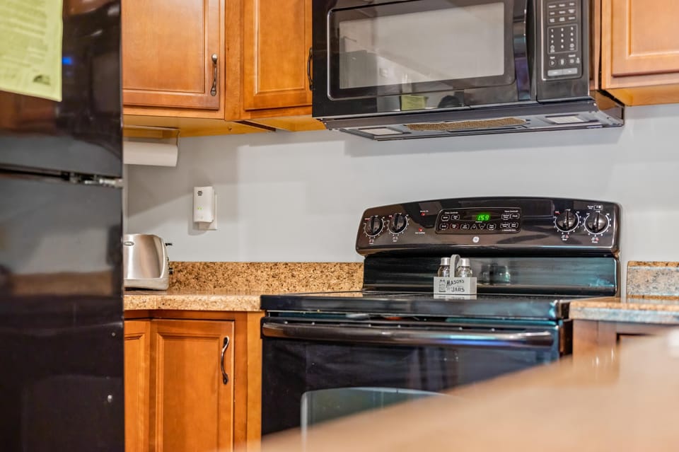 Black electric stove and microwave are set against honey-toned wooden cabinets and a speckled granite countertop.