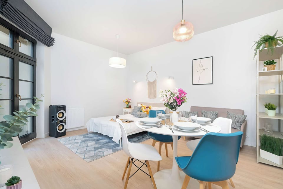 Bright living room with a comfortable sofa, a double bed, a dining area with blue chairs, large windows and modern lighting.