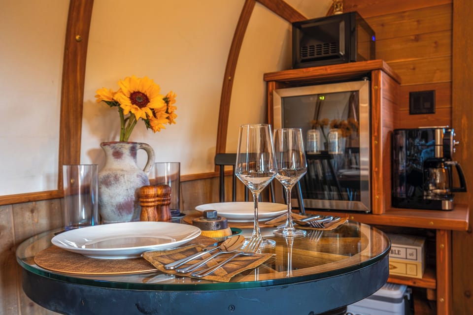 Dining setup for two with glassware, coffee station, beverage fridge, and board games nearby.