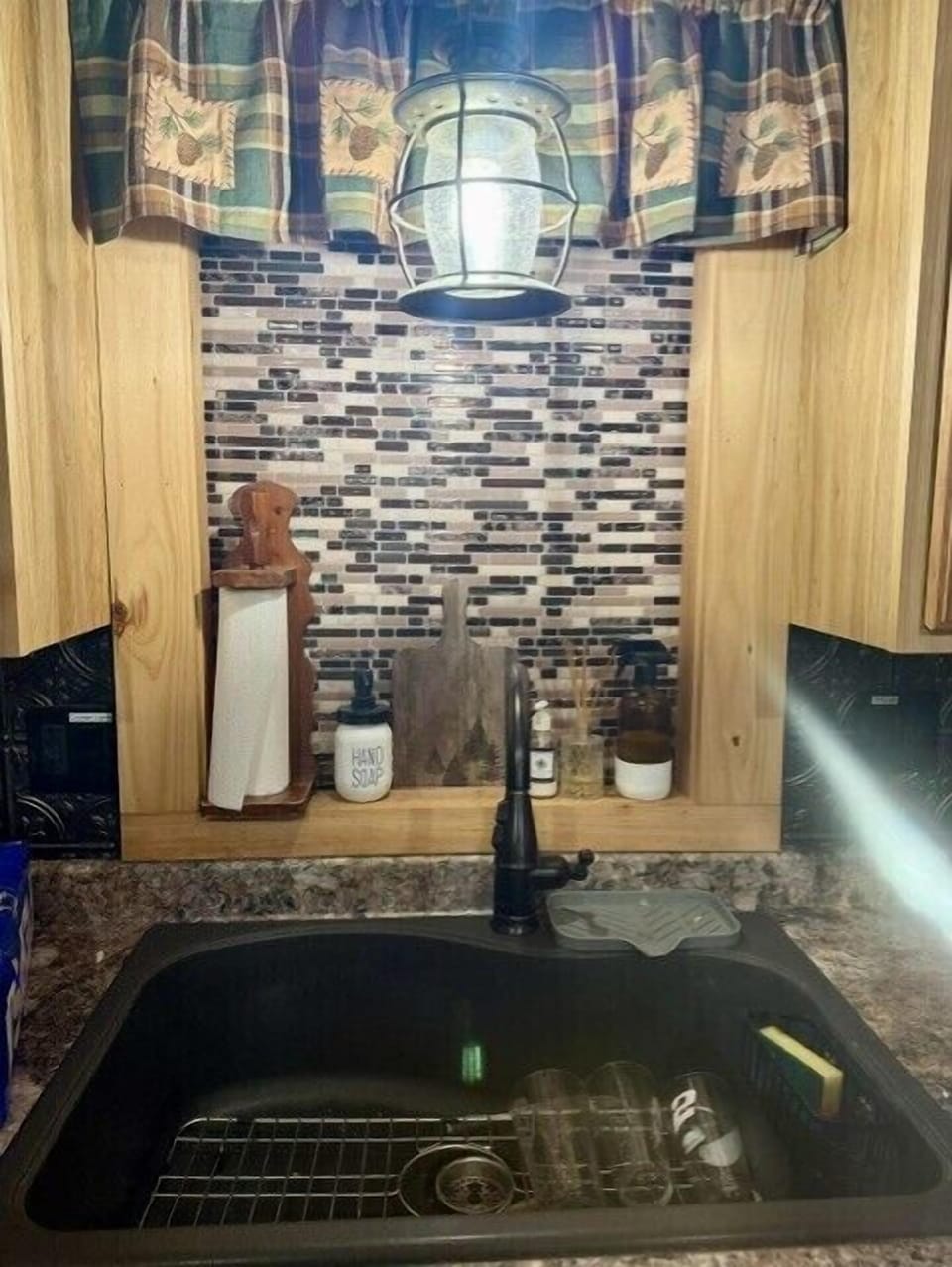 Cozy rustic kitchen nook with black sink, tile backsplash, and lantern light.