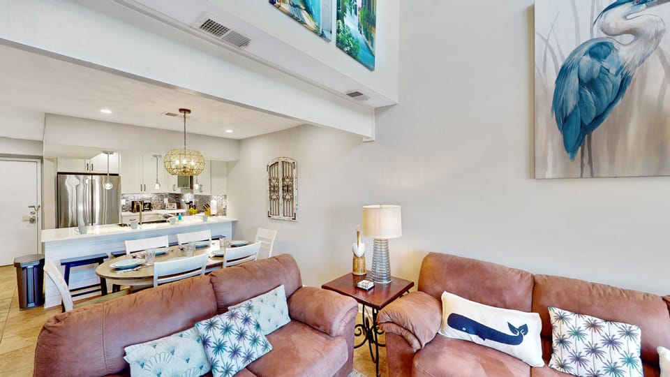 An open living space flows into a bright dining area and modern kitchen, creating a welcoming home-away-from-home. Soaring ceilings and coastal artwork add a sense of calm and space.