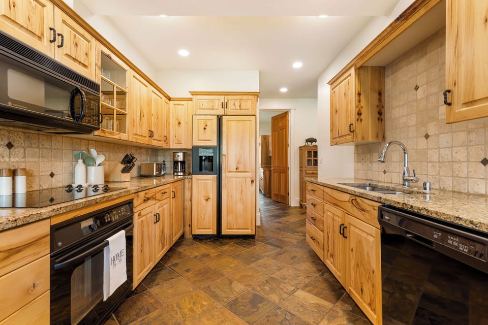 Fully equipped kitchen with warm wood cabinets and granite counters, modern appliances, and ample prep space perfect for gathering and cooking together.