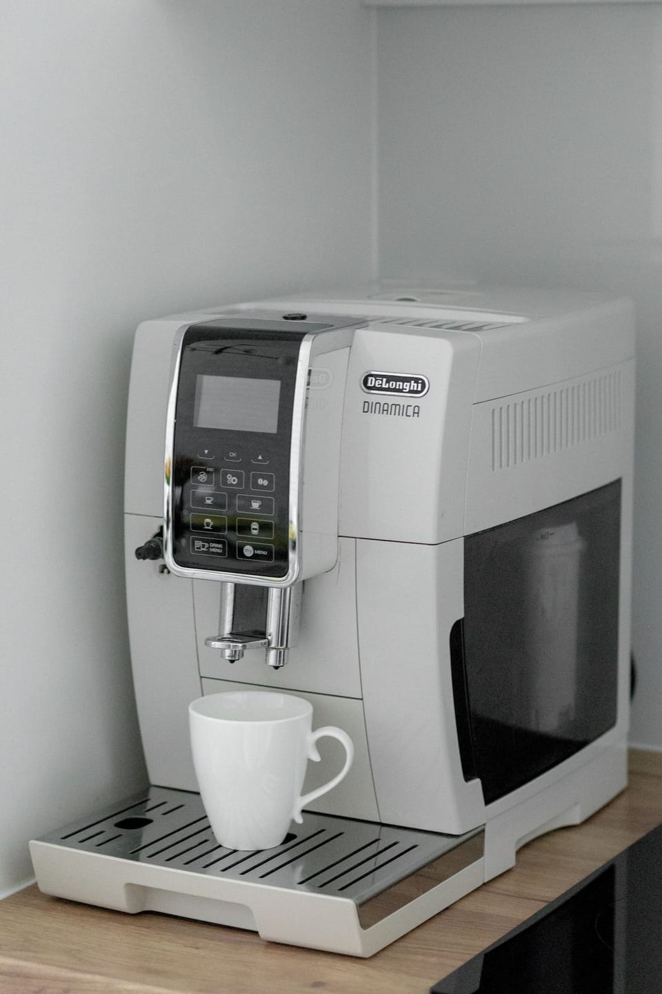 Close-up shot of an automatic coffee machine sitting on a countertop. A white coffee cup rests under the spout, ready for a fresh brew.