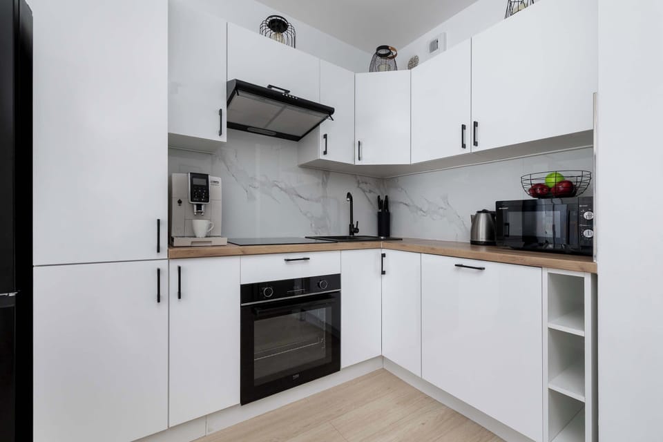 Compact corner kitchen design displaying upper and lower white cabinets paired with a wooden countertop. Built-in appliances include a black oven, cooktop, and range hood.