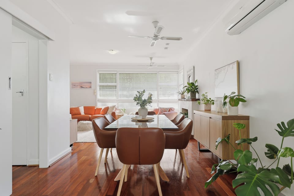 Gather around this sleek glass-top dining table set with warm leather seating, polished hardwood floors, climate control, and lush indoor greenery for memorable meals together!