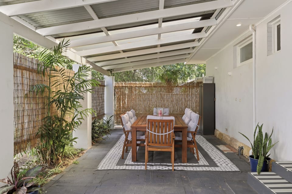 Enjoy alfresco meals year-round under the covered pergola, surrounded by lush potted palms and natural bamboo hedging.