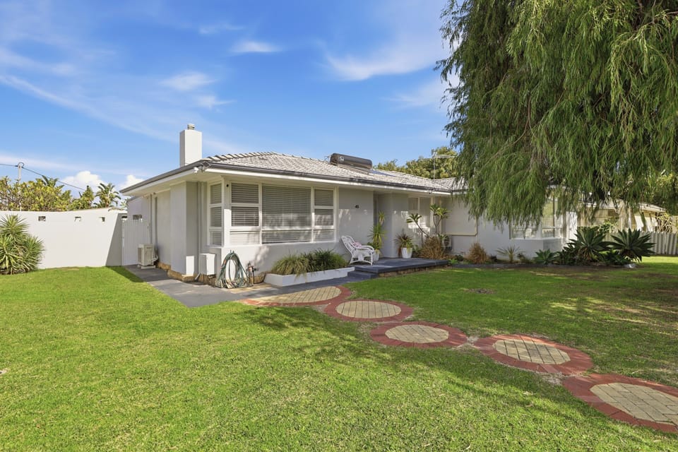 Charming coastal-style facade featuring lush green lawns, stepping stone pathways, and a bright, welcoming entrance.