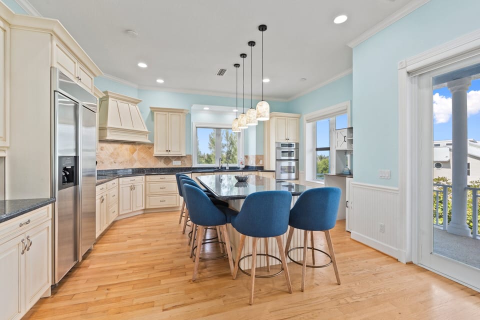 The kitchen features a large island with seating, stainless steel appliances, and a 3rd floor balcony view of sunsets over the Indian River Lagoon.