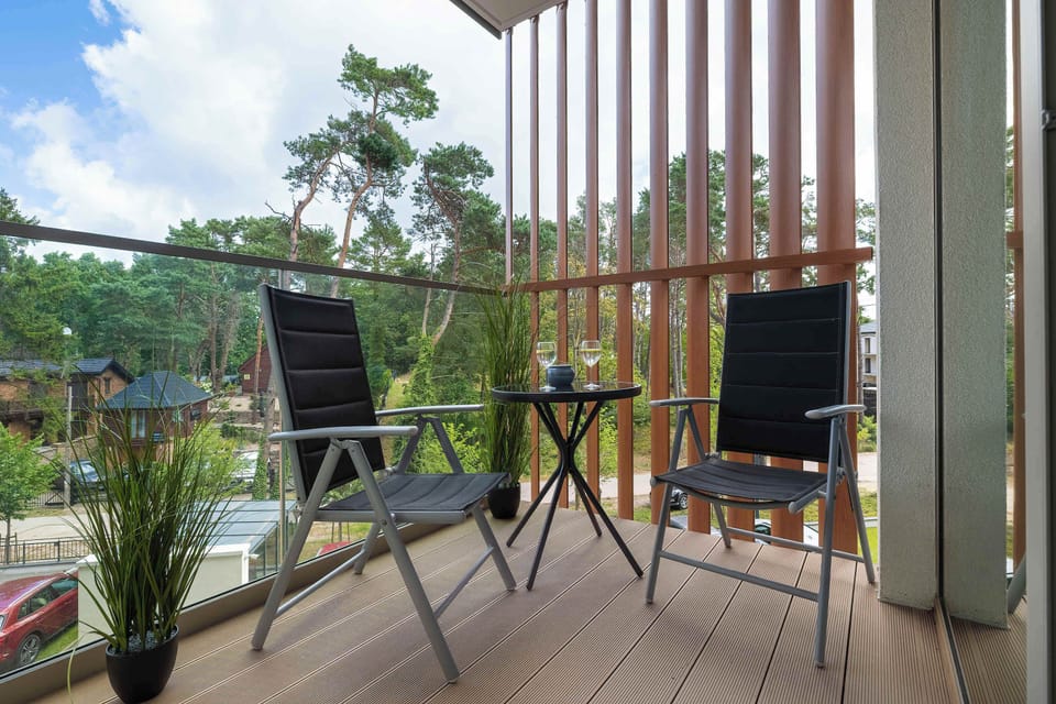 The balcony area is equipped with two adjustable patio chairs and a small table overlooking pine trees under a clear sky.