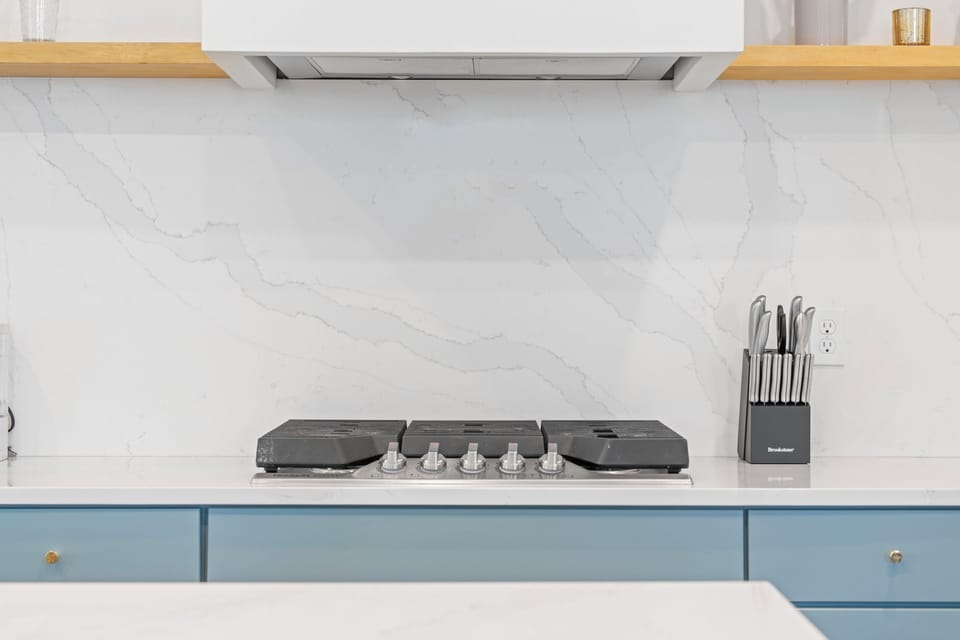 Five gas burners and a marble backsplash worth cooking in front of. Whether it is a big Sunday sauce or grilled cheese at midnight, this is where the family recipes get made and the house fills with something wonderful.