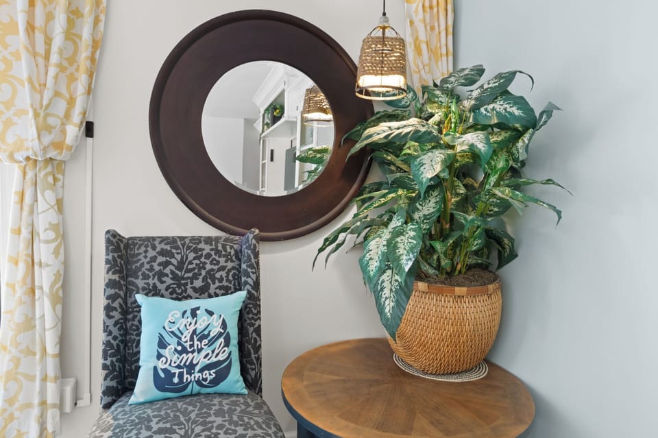 Settle into the cozy accent chair for a quiet moment, framed by a leafy plant and a warm woven pendant light.
