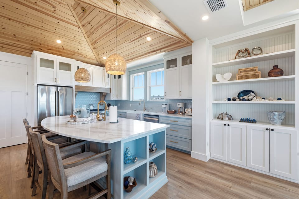 Step into your open, light-filled kitchen with vaulted wood ceilings, coastal-inspired blue cabinetry, and a spacious island perfect for gathering over morning coffee or casual meals.