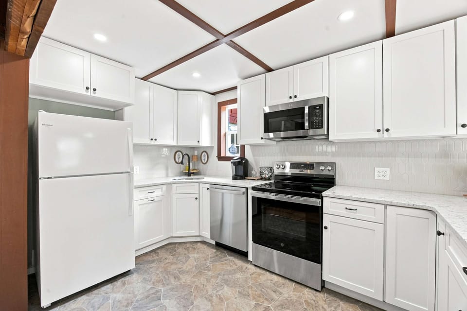 The renovated kitchen keeps things bright with white shaker cabinets, stainless appliances, and a picket-tile backsplash — fully stocked for cooking in.