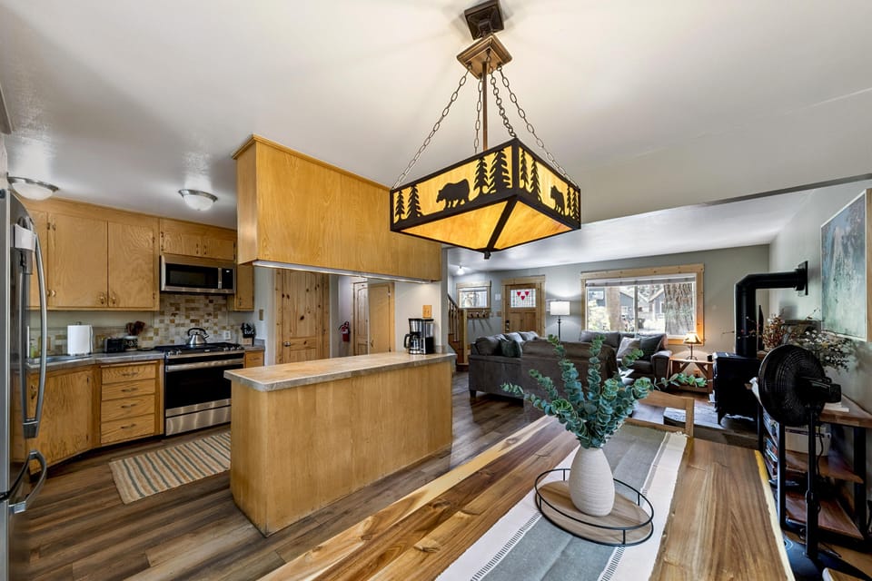 Wood-paneled kitchen with stainless appliances, a tiled backsplash, and a rectangular pendant light featuring bear and tree silhouettes.