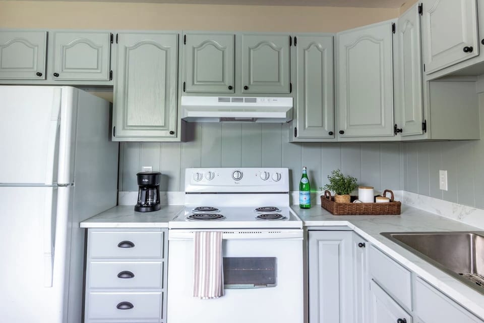 Classic white appliances and soft green cabinetry make the cook space feel bright and welcoming.