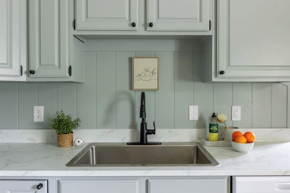 Sage cabinetry and a marble-look counter give the sink area a fresh, cheerful feel.
