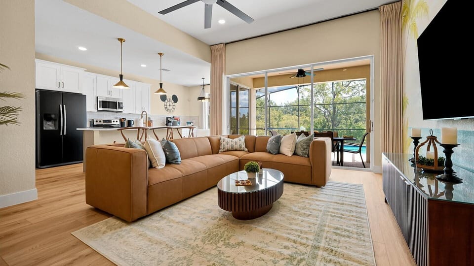 Living Room: Spacious open-concept living room with a large sectional, TV and direct access to the covered poolside lanai.