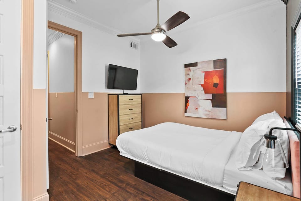 Inviting queen bedroom with a Smart TV, ceiling fan, hardwood floors, and colorful artwork.
