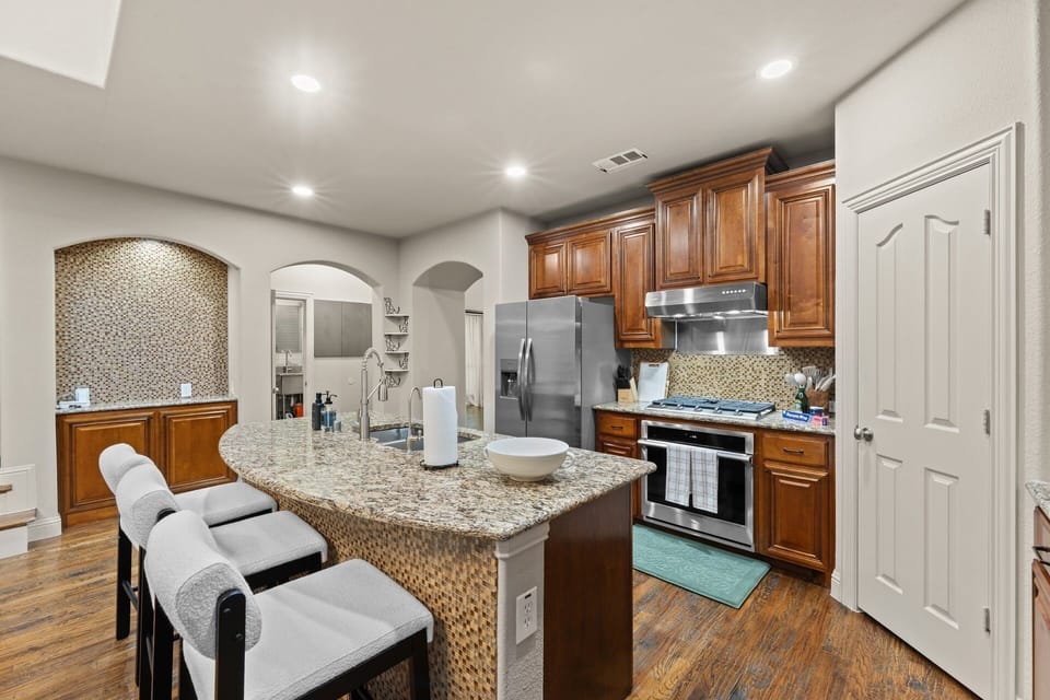 Cook with ease in the fully stocked kitchen featuring granite counters, stainless appliances, a gas cooktop, and island seating for casual mornings.